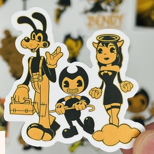 May include: A set of three cartoon character stickers featuring a black and white dog with a tool belt, a black and white devil with a halo, and a black and white cartoon character with a bow tie. The stickers are on a white background.