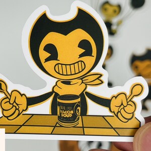 May include: A yellow cartoon character with black eyes and a black bow tie holding a spoon in each hand. The character is sitting at a table with a can of "Blue Label Bacon Soup" in front of them.