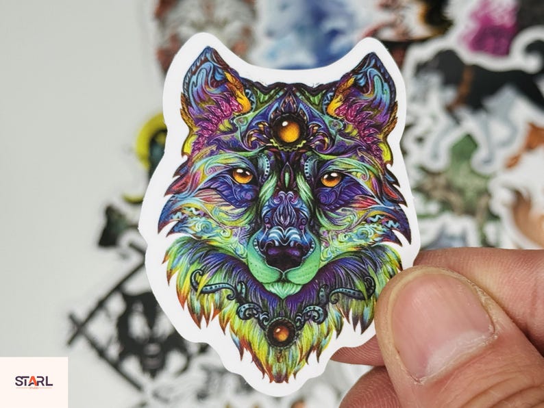May include: A colorful wolf sticker with intricate details. The wolf's face is depicted with vibrant hues of blue, purple, green, and yellow. The sticker has a white border and is held by a hand. The word "STARL" is visible in the lower left corner.