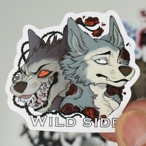 May include: A sticker featuring two wolf illustrations. One wolf is snarling with red eyes and exposed teeth, the other has a more neutral expression. Red roses and the words "WILD SIDE" are also included.