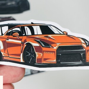 Puede incluir: Pegatina de coche naranja y negro con una ilustraci&oacute;n detallada de un coche deportivo. El coche tiene un gran aler&oacute;n trasero y un kit de carrocer&iacute;a ancho.