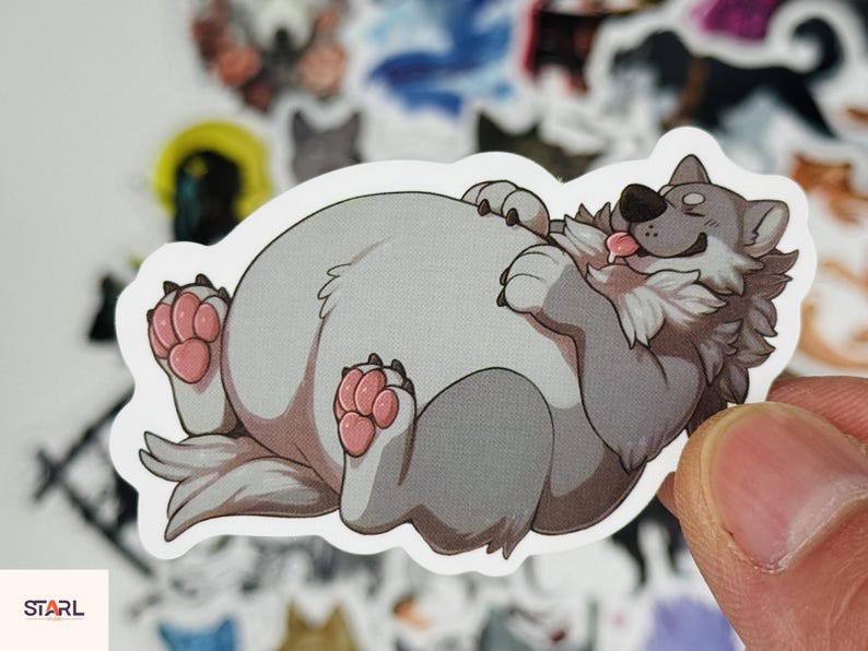 May include: A sticker featuring a cartoon wolf lying on its back with its tongue out. The wolf has gray fur, pink paws, and a happy expression. The sticker is white with a rounded edge. Other stickers are visible in the background.