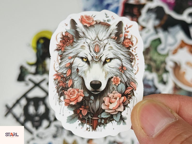 May include: A sticker featuring a detailed illustration of a wolf's face, adorned with roses and foliage. The wolf has yellow eyes and a decorative headpiece. The sticker has a white border and is held by a hand.