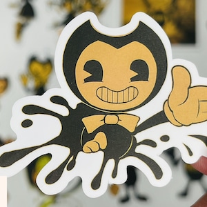 May include: A black and yellow cartoon character with a bow tie and a big grin, standing in a black ink splatter. The character is wearing a black suit and has large, white eyes.