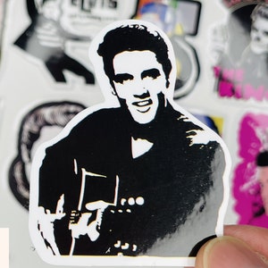 May include: Black and white sticker of a man playing a guitar. The man has a black silhouette with a white face and hair. The guitar is also a black silhouette with white details. The sticker is on a white background.