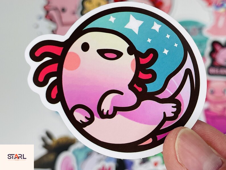 Op de afbeelding: Een roze en paarse axolotl sticker met een blauwe en witte sterrenachtergrond. De axolotl glimlacht en heeft een roze en rode kraag.