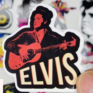 May include: A sticker featuring a black and white illustration of Elvis Presley playing a red electric guitar. The sticker has the word "ELVIS" in large, yellow letters.