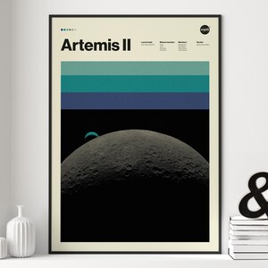 May include: A framed poster featuring the text "Artemis II" with a NASA logo. The artwork depicts a crescent moon against a black background, with horizontal stripes of teal and blue. The poster is in a black frame.