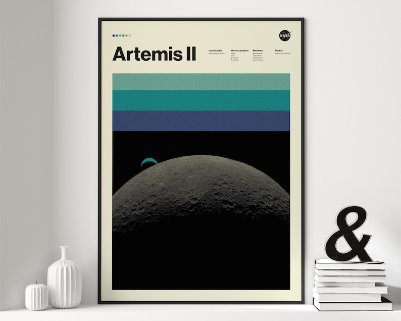May include: A framed poster featuring the text "Artemis II" with a NASA logo. The artwork depicts a crescent moon against a black background, with horizontal stripes of teal and blue. The poster is in a black frame.