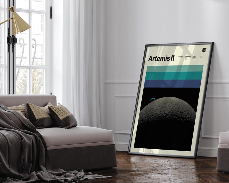 May include: A framed poster with the text "Artemis II" features a graphic of the moon and a blue and green striped design. The poster is leaning against a white wall in a room with a window and a couch.