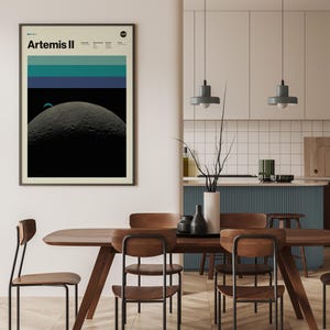 May include: Framed art print featuring the text "Artemis II" with a NASA logo. The artwork depicts a celestial scene with a large, textured moon in the foreground, a smaller planet, and horizontal bands of teal and blue above.