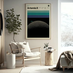 May include: A framed poster with the text "Artemis II" and a graphic of the moon. The poster has a beige border and is hanging on a light-colored wall. The room includes a wooden chair, side table, and a cabinet.