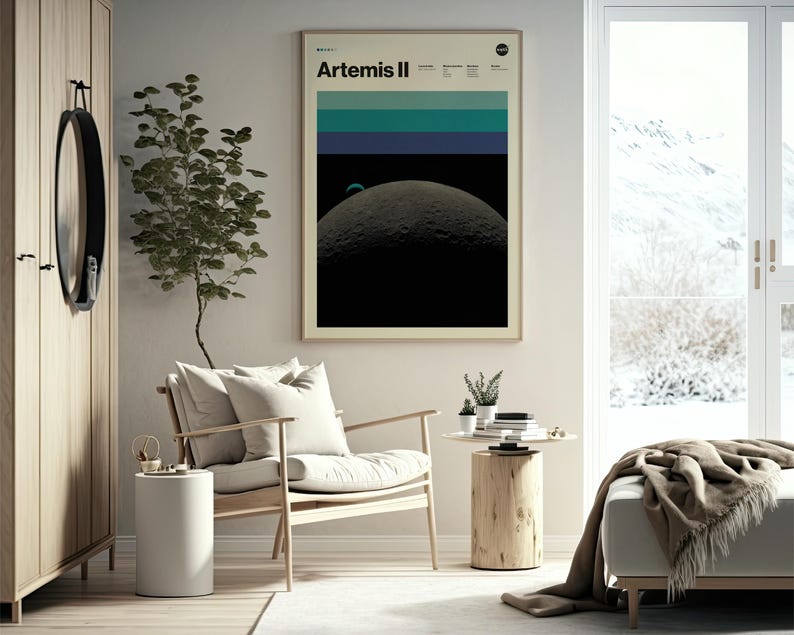 May include: A framed poster with the text "Artemis II" and a graphic of the moon. The poster has a beige border and is hanging on a light-colored wall. The room includes a wooden chair, side table, and a cabinet.