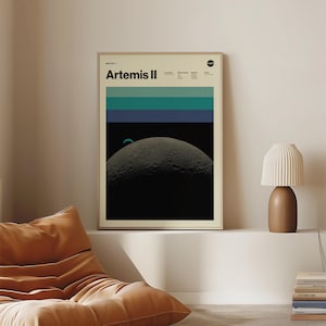 May include: A framed poster with the text "Artemis II" at the top. The poster features a graphic of the moon with a blue and green striped design above it. The poster is in a room with a lamp and a beanbag chair.