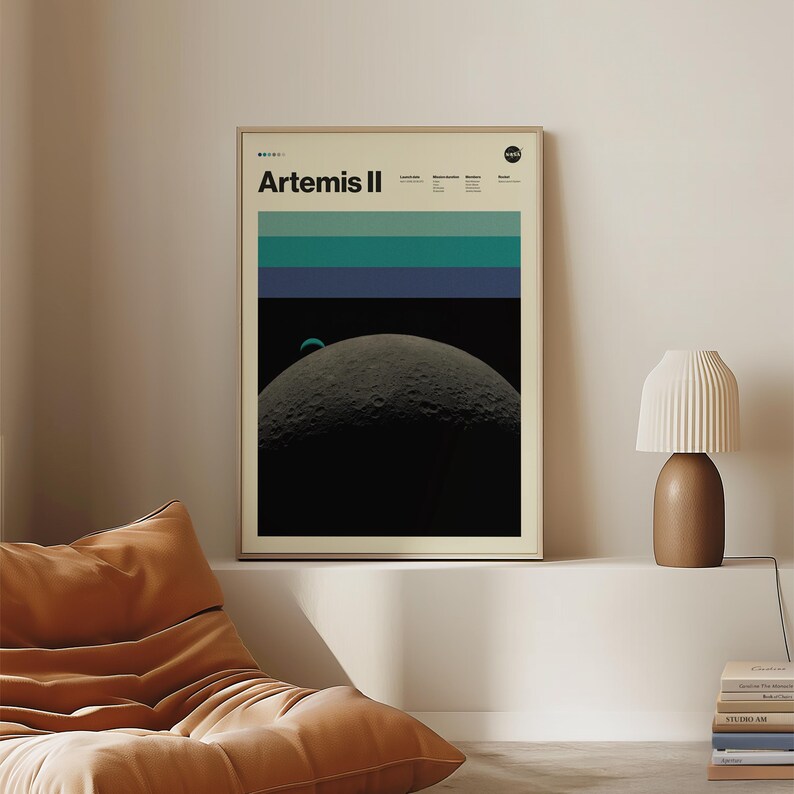 May include: A framed poster with the text "Artemis II" at the top. The poster features a graphic of the moon with a blue and green striped design above it. The poster is in a room with a lamp and a beanbag chair.