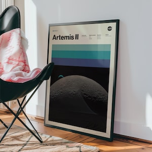 May include: Framed poster featuring the Artemis II mission. The poster has a black frame and displays the mission name, a series of horizontal blue and teal stripes, and a detailed image of the moon's surface. The NASA logo is visible in the top right corner.