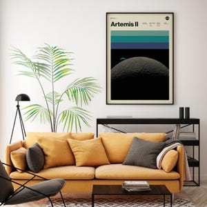 May include: A framed poster with the text "Artemis II" at the top. The poster features a design with horizontal bands of teal and blue above a depiction of a gray, cratered moon against a black background. The poster is displayed above a yellow sofa.