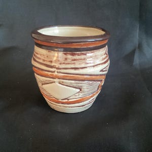 May include: A white ceramic pot with brown and orange geometric designs. The pot has a rounded shape and a wide opening.