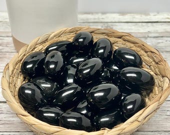 May include: A woven basket filled with smooth, black obsidian tumbled stones. The stones are polished and have a glossy finish.
