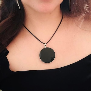 May include: A black pendant necklace with a round, black stone pendant. The necklace is on a black leather cord.