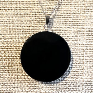 May include: A black pendant necklace with a round, smooth, black stone. The necklace is made of silver chain.