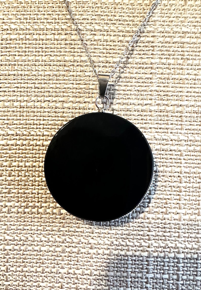 May include: A black pendant necklace with a round, smooth, black stone. The necklace is made of silver chain.