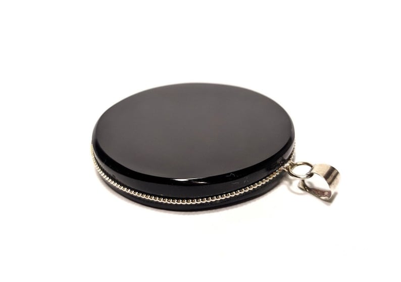 May include: A black round pendant with a silver beaded edge and a silver bail.