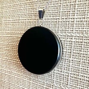 May include: A black onyx pendant on a silver chain. The pendant is round and has a smooth, polished surface.