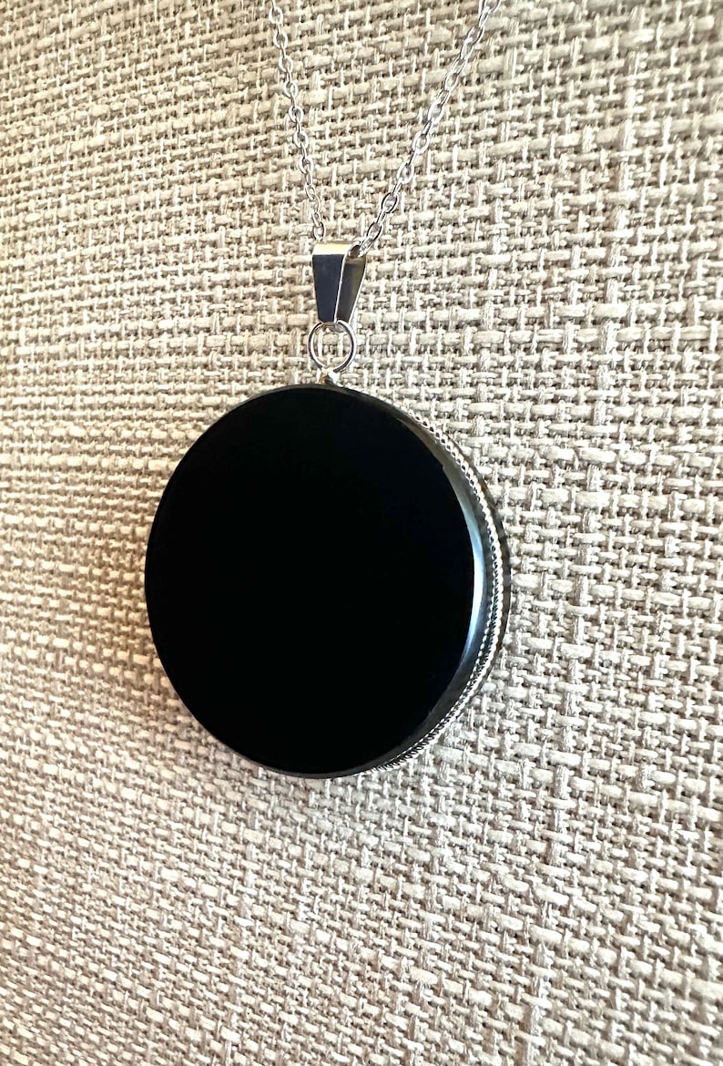 May include: A black onyx pendant on a silver chain. The pendant is round and has a smooth, polished surface.