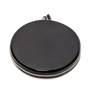 May include: Black round pendant with a silver beaded border. The pendant has a smooth, polished surface.