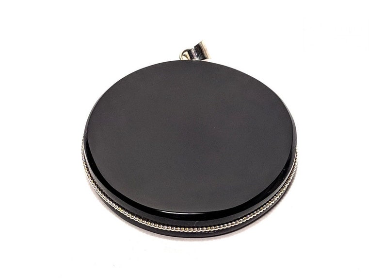 May include: Black round pendant with a silver beaded border. The pendant has a smooth, polished surface.