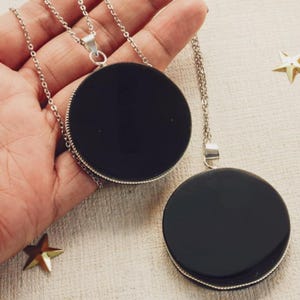 May include: Two black round pendants on silver chains. The pendants are smooth and have a shiny finish.