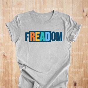 May include: A gray t-shirt with the word "FREEDOM" printed on it in colorful letters. The letters are in a box with a blue outline.