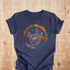 May include: A navy blue t-shirt with a graphic of a hand making the American Sign Language sign for "I love you". The hand is surrounded by a circle with the words "Advocate", "Inclusion", "Equity", "Accept", "Love", and "Kindness" in a rainbow color scheme.