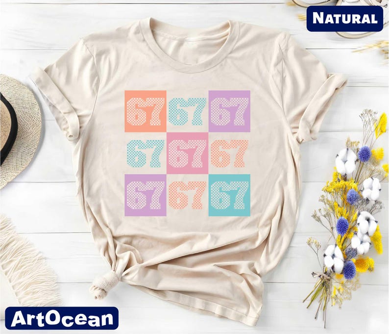 a beige t-shirt with a colorful graphic design of numbers on it, placed on a white surface alongside a hat and some flowers.