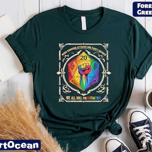 May include: Forest green t-shirt featuring a colorful graphic of a die with a fist inside. The text reads "When someone attacks one party member, we all roll for initiative." The shirt is paired with sneakers and a coffee cup.