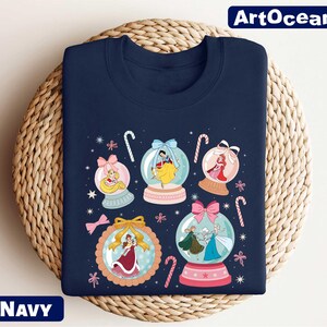 A navy blue t-shirt with a colorful graphic design featuring snowglobes and various Disney princess characters.