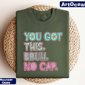 May include: A green t-shirt with the text "You got this.  Bruh. No cap." in colorful letters with a wavy, floral design.