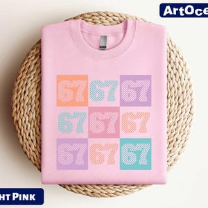 A pink t-shirt with the numbers '67676767' printed on it, displayed on a woven basket.