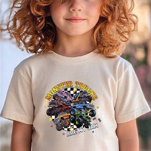 A young girl with curly hair wearing a white t-shirt with a graphic of monster trucks.