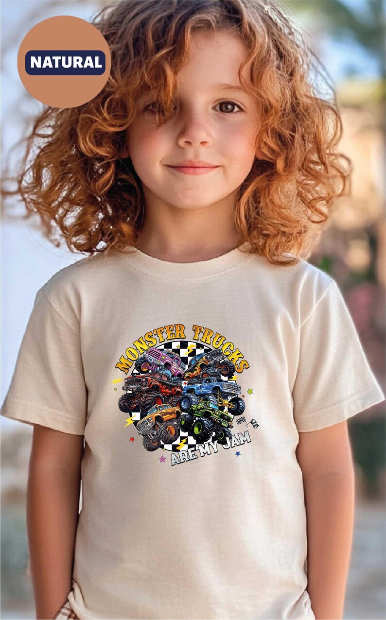A young girl with curly hair wearing a white t-shirt with a graphic of monster trucks.