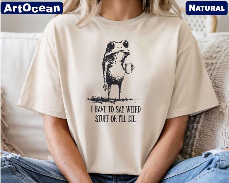 A person wearing a white t-shirt with a black and white illustration of a frog holding a cup and the text "I HAVE TO SAY WEIRD STUFF OR I'll die" printed on it.