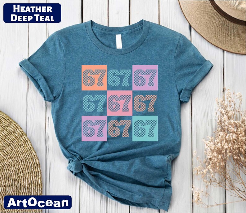 A blue t-shirt with a colorful graphic design of numbers on it, placed on a wooden surface alongside a hat and some dried flowers.