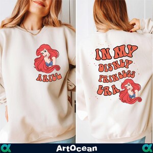 a woman wearing a white sweatshirt with the words i'm my disney princess ariel