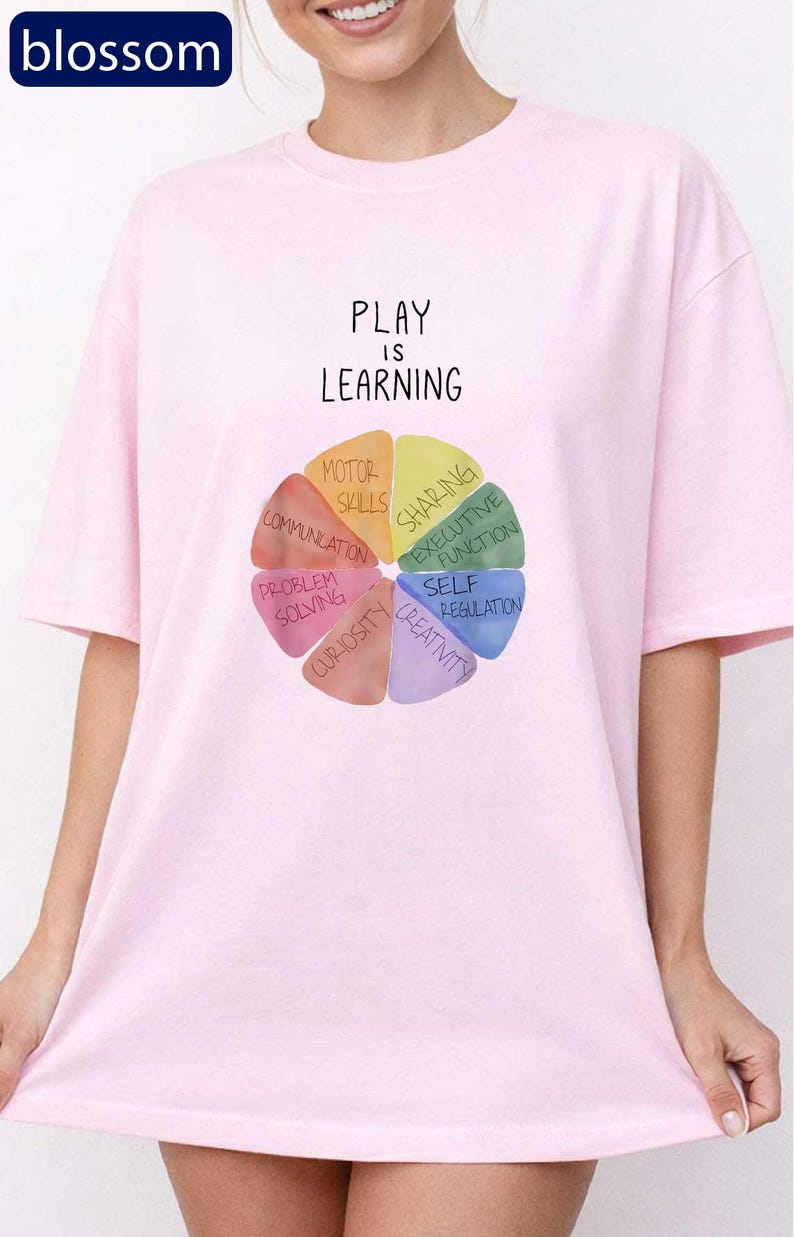 A woman wearing a pink t-shirt with a colorful wheel graphic and the text "PLAY IS LEARNING" printed on it.