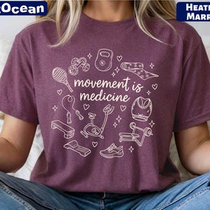 A person wearing a purple t-shirt with a graphic design featuring various fitness-related items and the text "motion is medicine".
