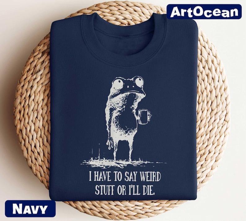 A navy blue t-shirt with a white illustration of a frog and the text "I HAVE TO SAY WEIRD STUFF OR ILL die" printed on it.