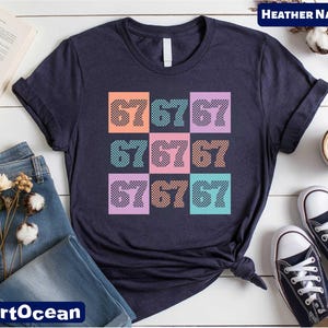 a navy blue t-shirt with a colorful graphic design of numbers on it, along with some casual clothing items such as jeans and sneakers, and a book.