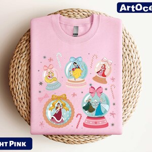 A pink t-shirt with a design featuring various cartoon characters and snow globes.
