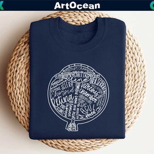 May include: A navy blue t-shirt with a white graphic of a human eye with the anatomical parts labeled. The graphic includes the words "ciliary", "anterior chamber", "trabecular meshwork", "crystalline lens", "ora serrata", "vitreous chamber", "choroid", "retina", "cones", "optic disc", "posterior pole", "macula", "fovea", and "retinal pigment epithelium".